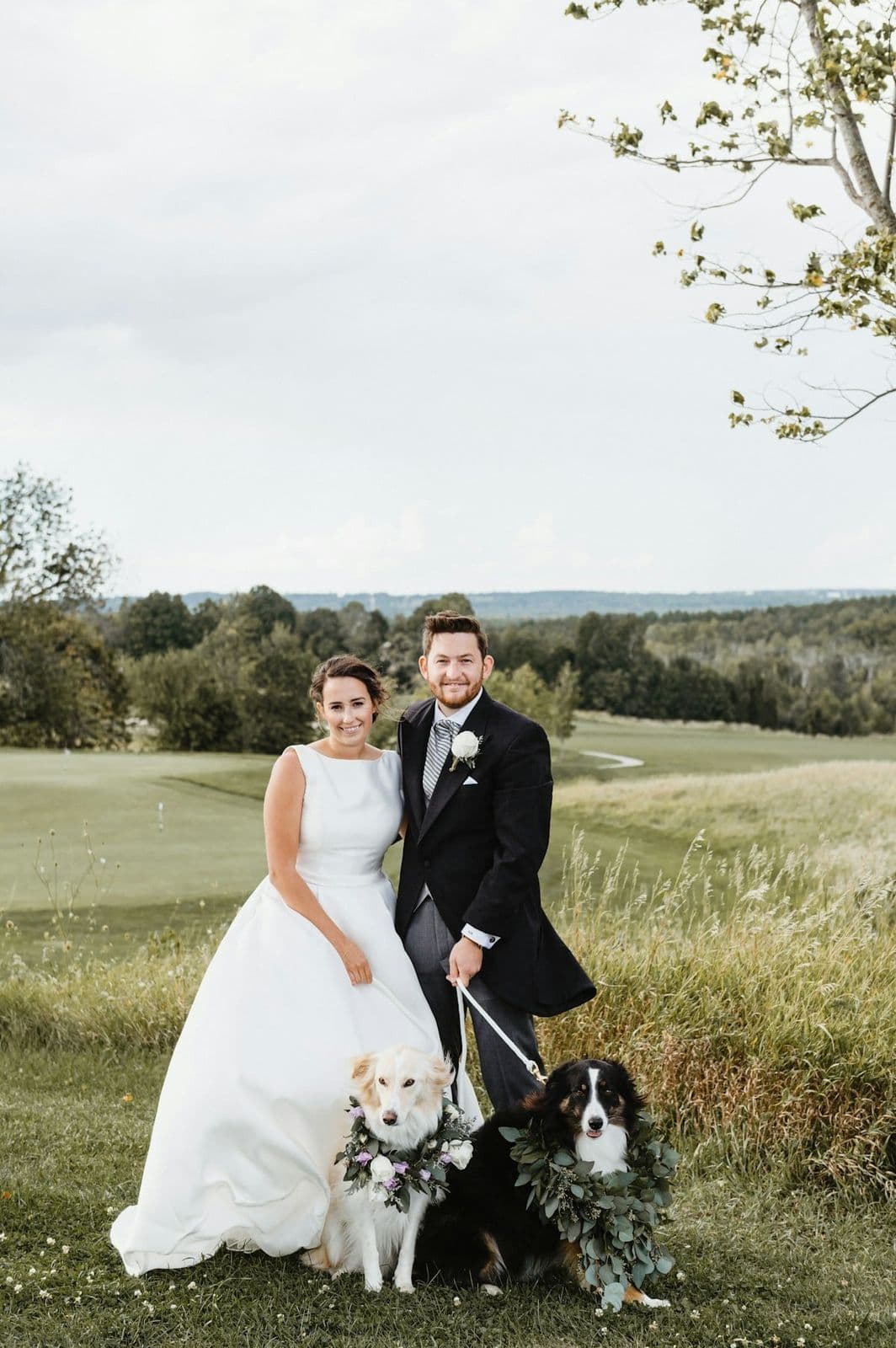 A newlywed couple with their two dogs in floral collars on their wedding day